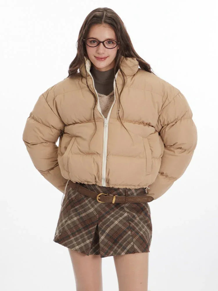 Front view of a woman wearing a beige cropped puffer jacket with a white zipper.