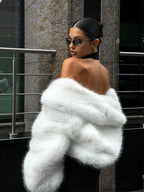 Woman with pink hair wearing a cream faux fur cropped jacket and a white knit hat.