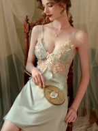 Woman holding a vintage hand mirror while wearing a light green satin slip dress with lace detailing.