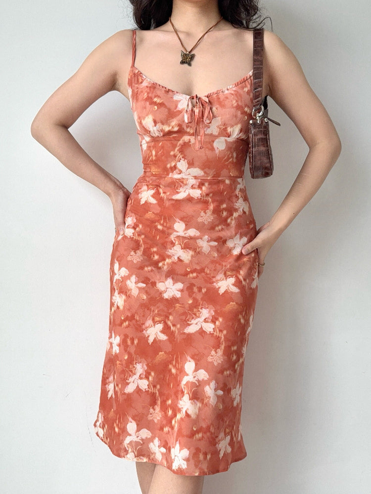 Woman wearing an orange floral print midi dress with spaghetti straps and a tie front detail.