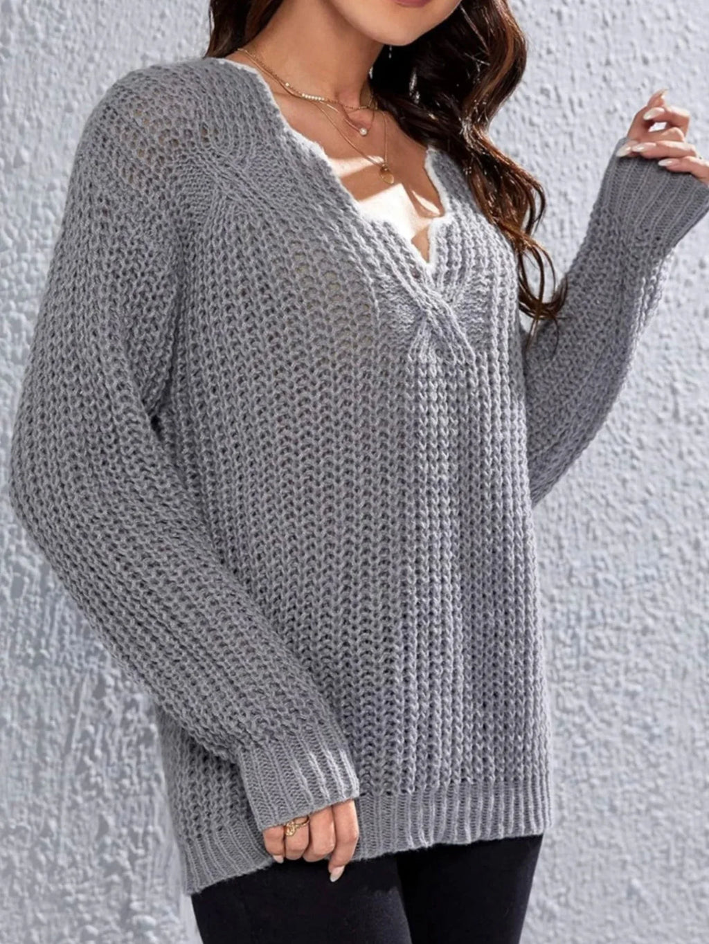 Woman wearing a grey knit V-neck sweater with textured pattern and long sleeves.