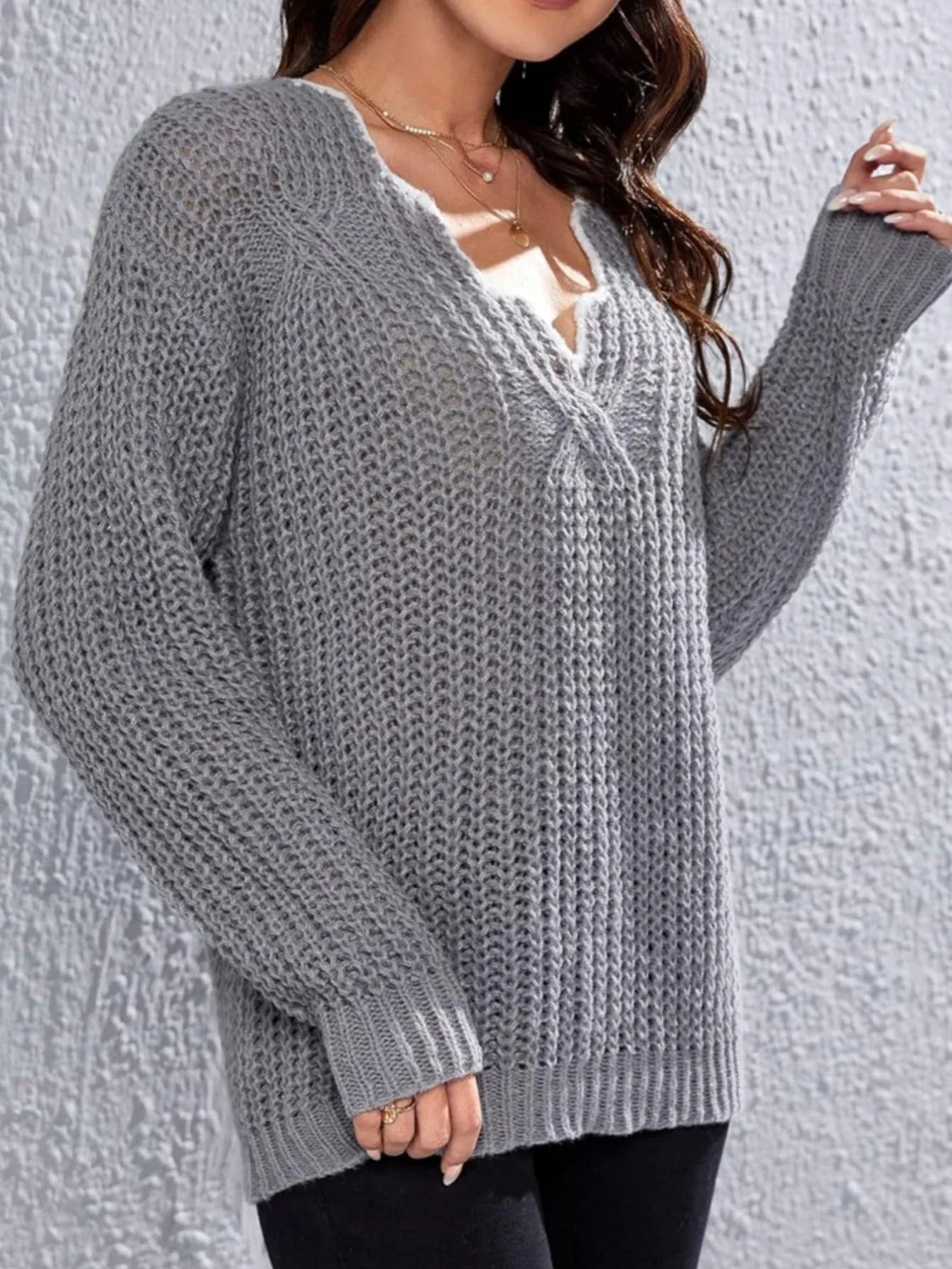 Woman wearing a grey knit V-neck sweater with textured pattern and long sleeves.