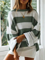 Woman in a green and white striped oversized knit sweater with crew neck and long cuffed sleeves, arm crossed.