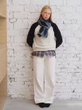 Model showcasing a cream and black sweater with contrasting sleeves, layered over a plaid shirt, paired with white pants and a blue argyle scarf.