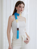 Woman in a white ribbed tank top and cream pants, styled with a long, fuzzy, color-blocked scarf.