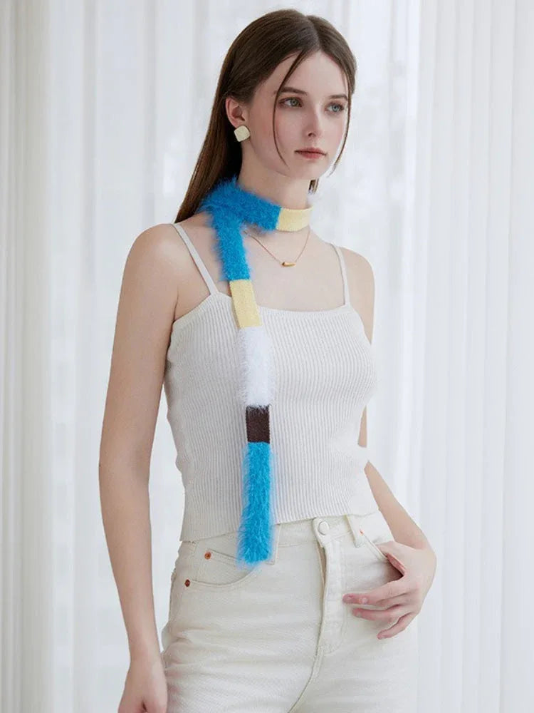 Woman in a white ribbed tank top and cream pants, styled with a long, fuzzy, color-blocked scarf.