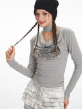 Model touching her braided hair, wearing a grey long-sleeve graphic t-shirt with a choker detail and silver ruffled shorts.