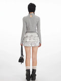 Back view of a model wearing a grey long-sleeve graphic t-shirt with a keyhole detail at the back and silver ruffled shorts.