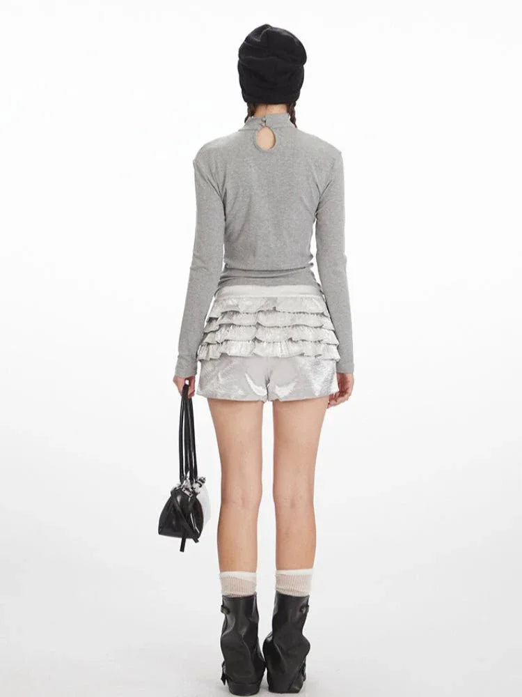Back view of a model wearing a grey long-sleeve graphic t-shirt with a keyhole detail at the back and silver ruffled shorts.