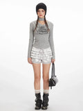 Model wearing a grey long-sleeve graphic t-shirt with a choker detail and silver ruffled shorts.