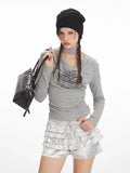 Close-up of a model wearing a grey long-sleeve graphic t-shirt with a choker detail and silver ruffled shorts, holding a black handbag.
