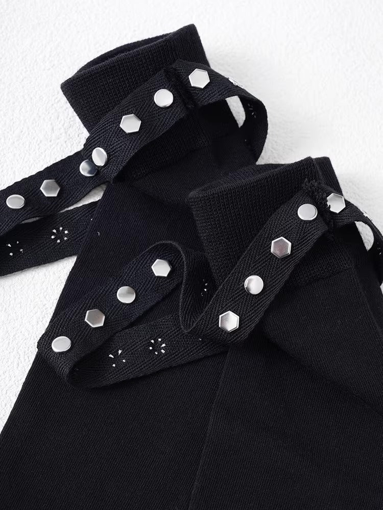 Detail view of the top cuff of black knee-high socks, showing knit texture, stud embellishments, and a strap with hexagonal studs.