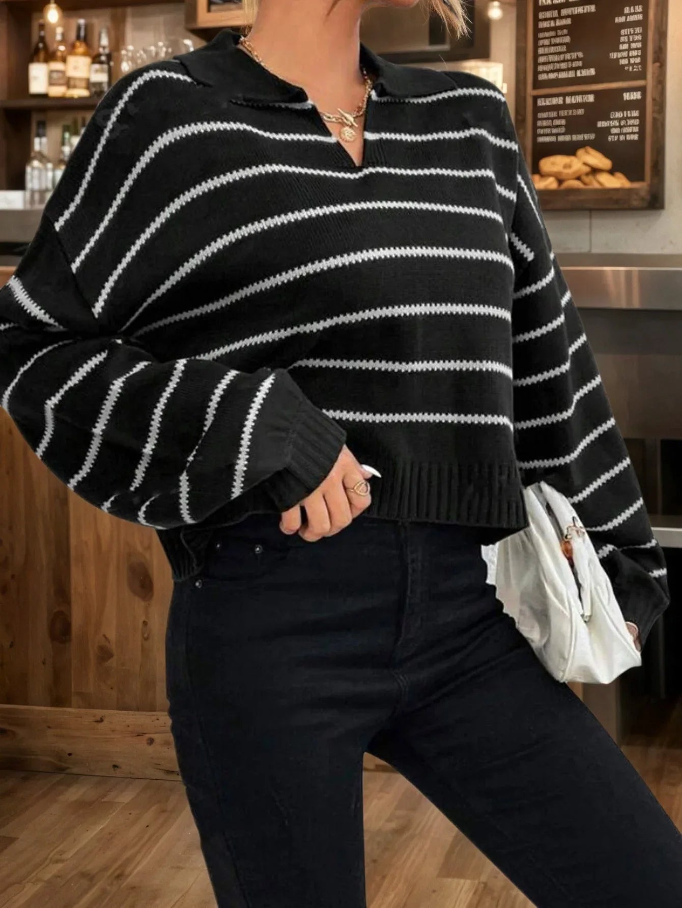Woman with a white clutch bag wearing a black and white striped cropped knit sweater.