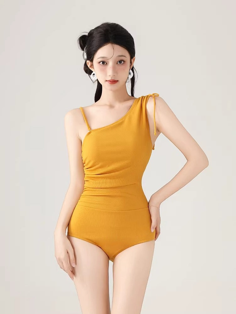 Front view of a woman wearing a yellow one-shoulder ribbed knit bodysuit with adjustable drawstring details