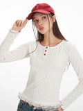 Woman adjusting her red baseball cap, wearing a white long-sleeve top with a red floral print and red trim.