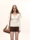 Woman wearing a cream long-sleeve top with lace trim and a bow detail, brown shorts, and a brown shoulder bag.