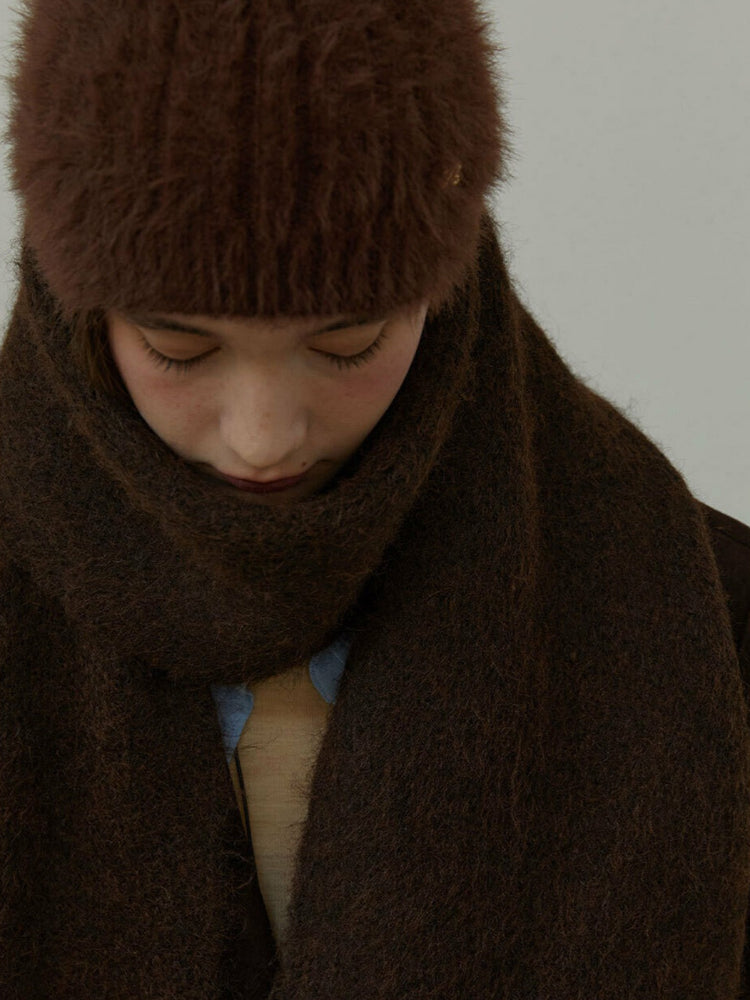 Model wearing a brown knit scarf draped over a dark brown blazer