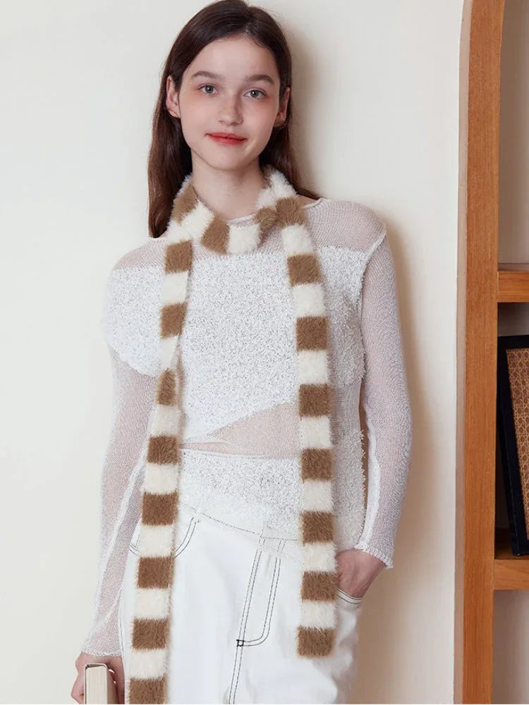 Woman posing with a brown and white striped fuzzy scarf around her neck, paired with a white top and white pants.