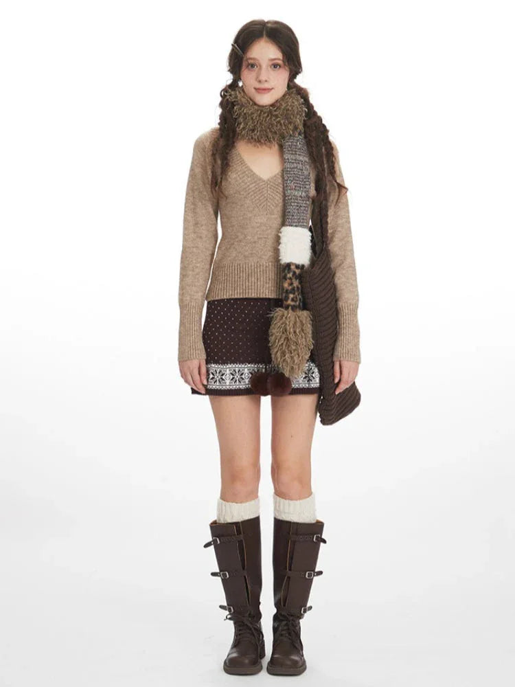 Woman wearing a beige V-neck knit sweater with long sleeves, paired with a brown patterned skirt, white socks, and brown boots.