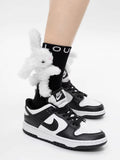 Black crew socks with a plush white bunny charm and 'LOU' logo, worn with black and white sneakers.
