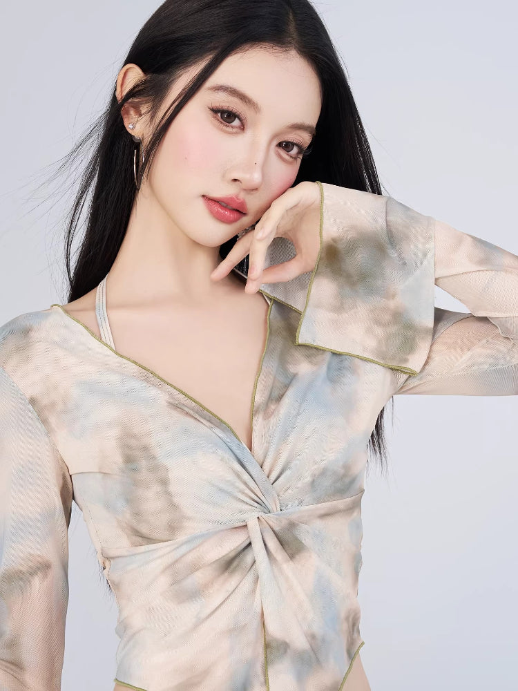 Woman wearing a long-sleeved sheer mesh top with a tie-front detail and a matching abstract print mini skirt.
