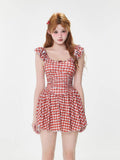 Woman wearing a red and white gingham dress with ruffled sleeves and a bow accent