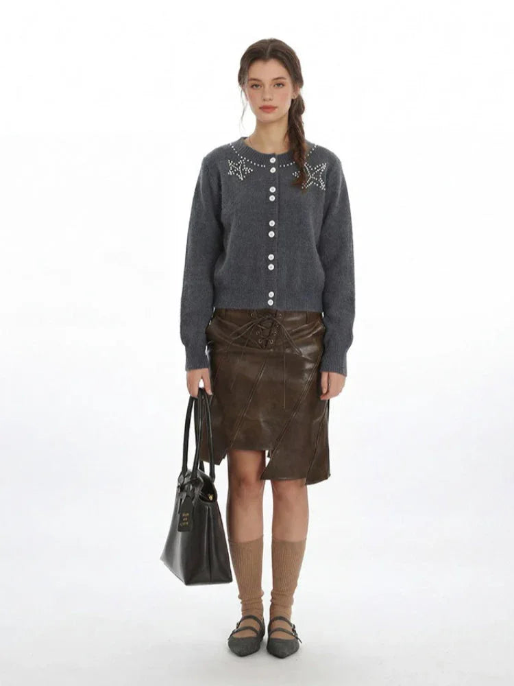 Woman wearing a grey knit cardigan with pearl embellishments and a brown faux leather skirt. Main image