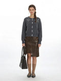 Woman wearing a grey knit cardigan with pearl embellishments and a brown faux leather skirt.