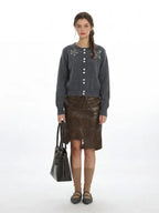 Woman wearing a grey knit cardigan with pearl embellishments and a brown faux leather skirt.