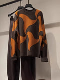 A brown and orange abstract patterned knit sweater hanging on a rack with dark pants.