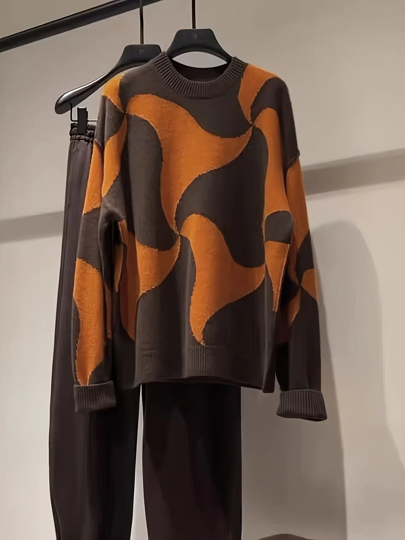 A brown and orange abstract patterned knit sweater hanging on a rack with dark pants.
