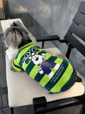 Miniature schnauzer wearing a green and dark green striped dog t-shirt with a cartoon dog graphic and text on the back.