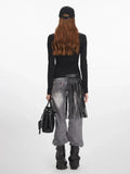 Back view of a woman wearing a black long-sleeve zip-up top with graphic print, grey wide-leg jeans with fringe detail, black boots, and black baseball cap.