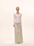 Full-body shot of a model in a light pink long-sleeve top and a beige maxi skirt.