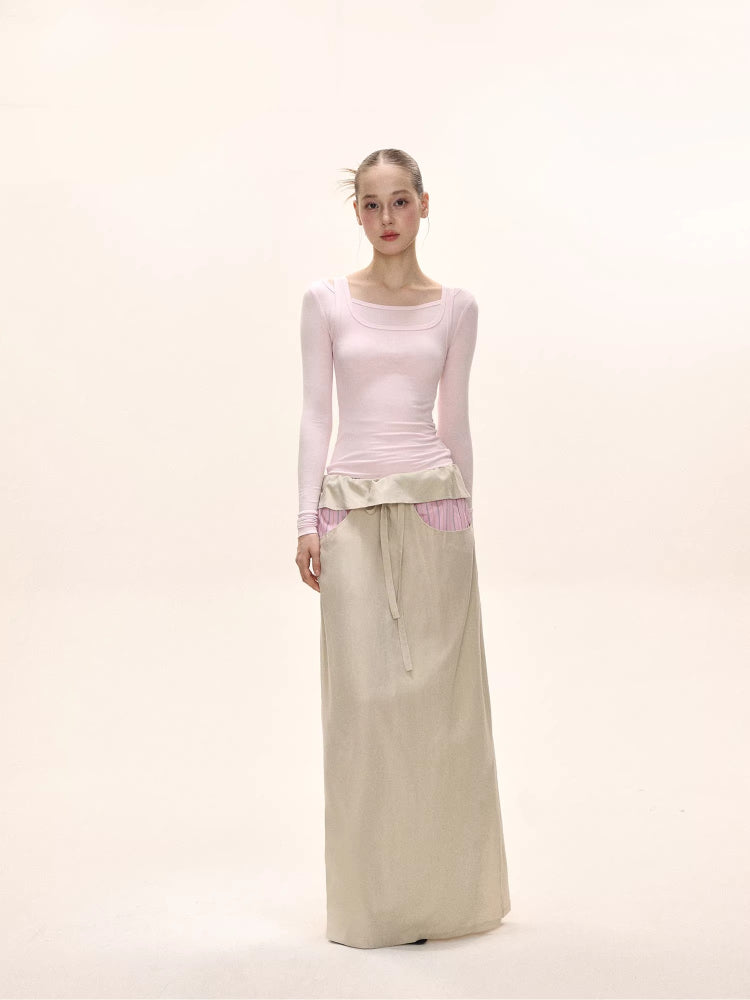 Full-body shot of a model in a light pink long-sleeve top and a beige maxi skirt.