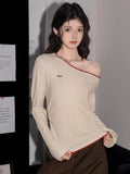 Woman wearing a cream long-sleeve top with an asymmetrical neckline and red trim, with one shoulder exposed.