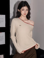 Woman wearing a cream long-sleeve top with an asymmetrical neckline and red trim, with one shoulder exposed.
