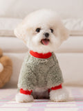 A white Bichon Frise dog wears a light green fleece dog sweater with red accents and an embroidered pattern.