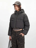 Model showcasing a cropped grey puffer jacket with a hood and silver zipper details.