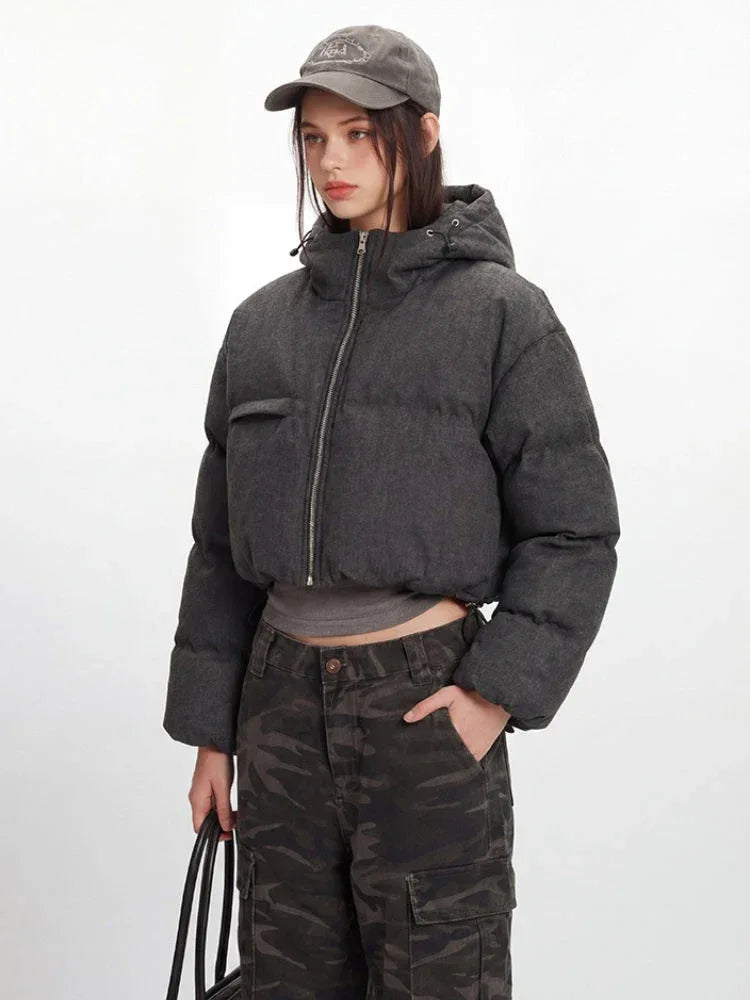 Model showcasing a cropped grey puffer jacket with a hood and silver zipper details.