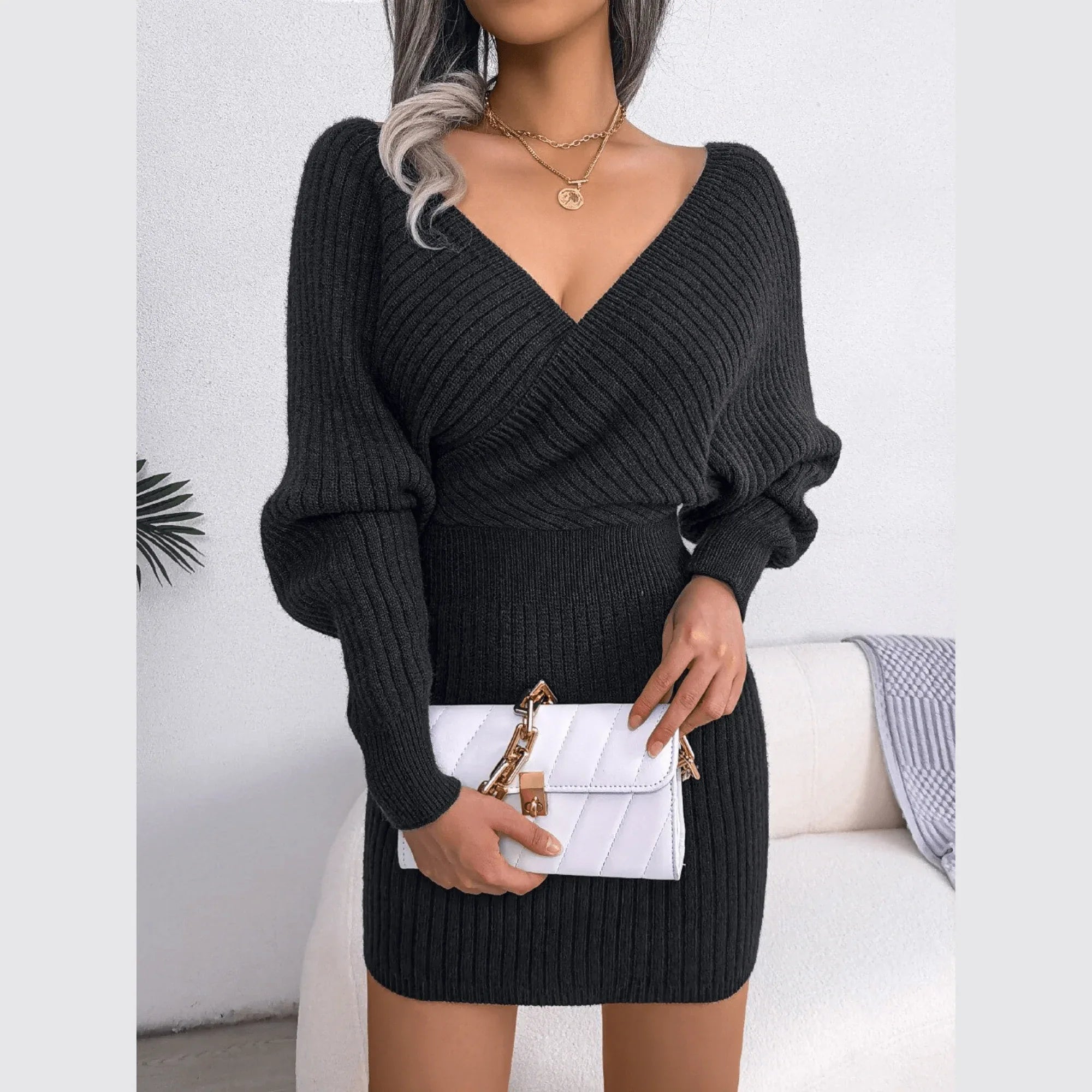 Woman holding a white quilted handbag wearing a charcoal grey long-sleeved V-neck wrap knit dress.