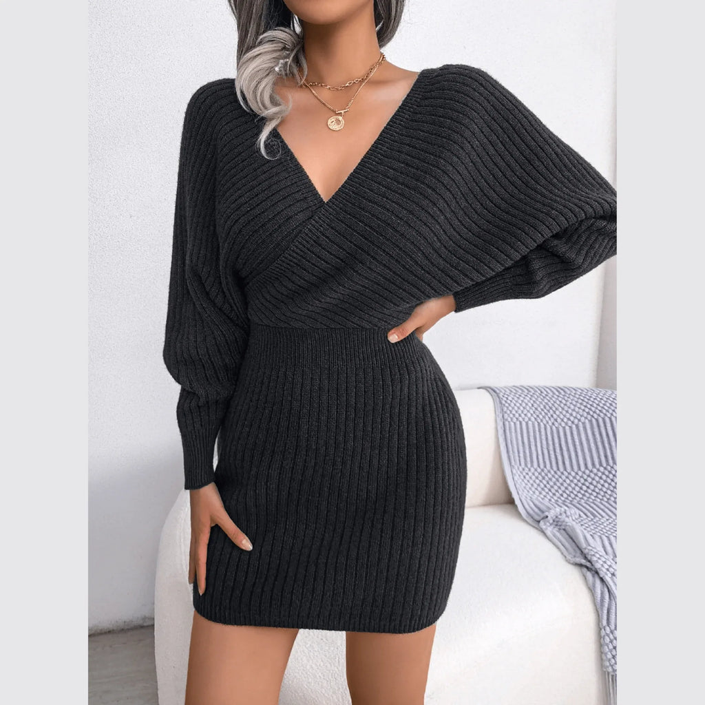 Woman with one hand on hip wearing a charcoal grey long-sleeved V-neck wrap knit dress.