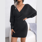Woman with one hand on hip wearing a charcoal grey long-sleeved V-neck wrap knit dress.