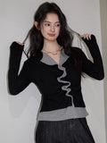 Woman in a black and grey layered top with ruching, posing with hands in hair.