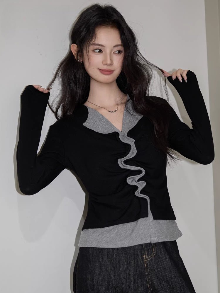 Woman in a black and grey layered top with ruching, posing with hands in hair.