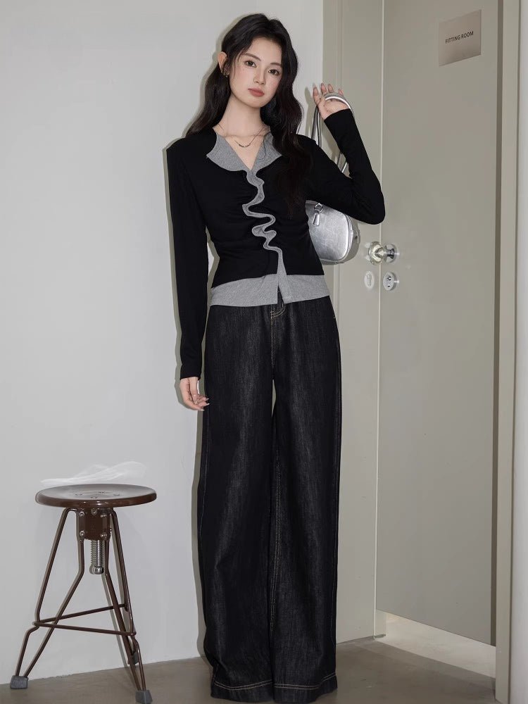 Full body shot of a woman in a black and grey layered top, dark wash wide-leg jeans, and a silver handbag.