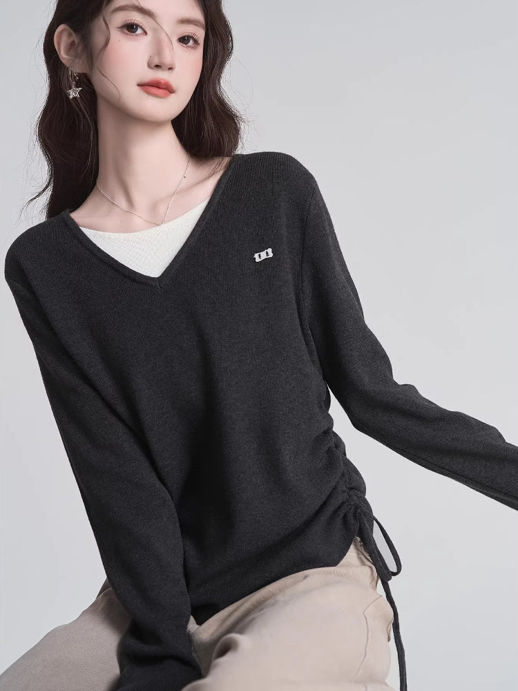Close-up of a woman wearing a dark grey v-neck knit sweater with ruched sides.