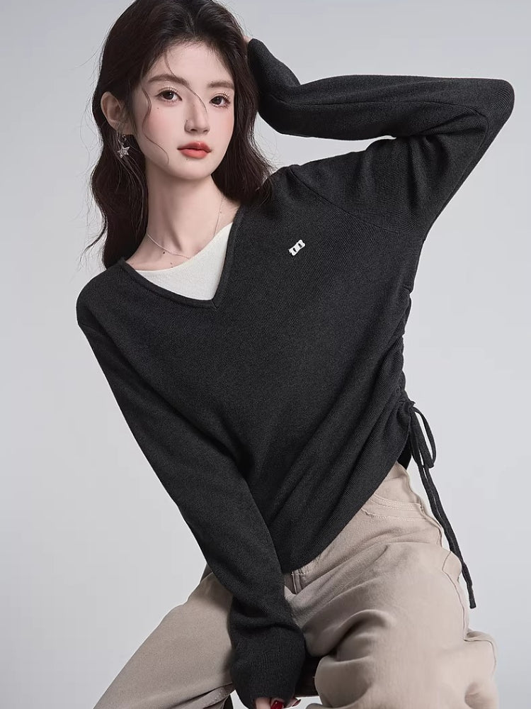 Woman wearing a dark grey v-neck knit sweater with ruched sides and a white undershirt.