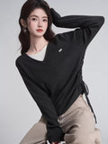 Woman wearing a dark grey v-neck knit sweater with ruched sides and a white undershirt.