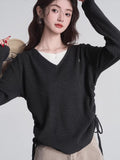 Woman in a dark grey v-neck knit sweater with ruched sides, layered over a white shirt.